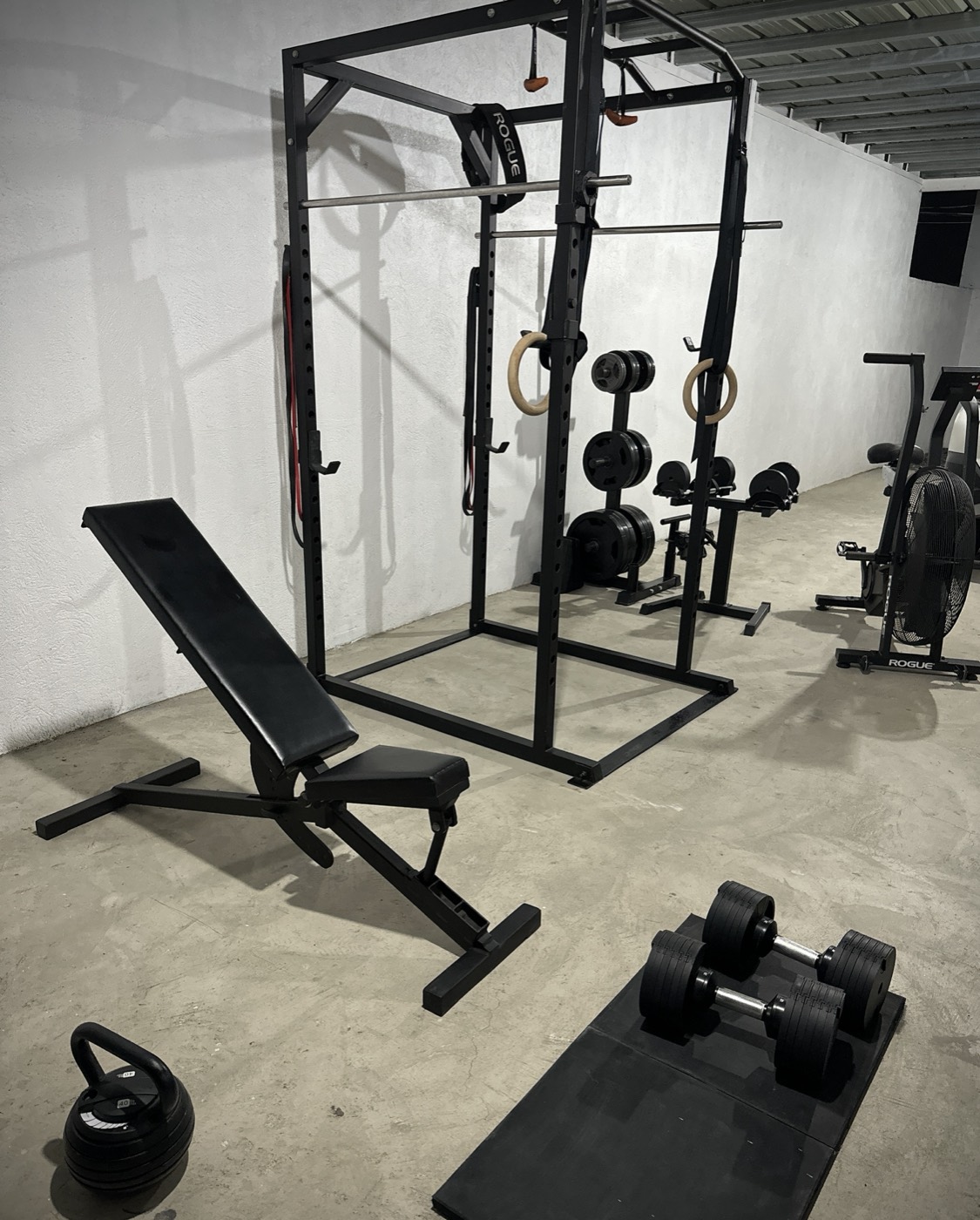 John Arce's home gym setup with a squat rack and rowing machine