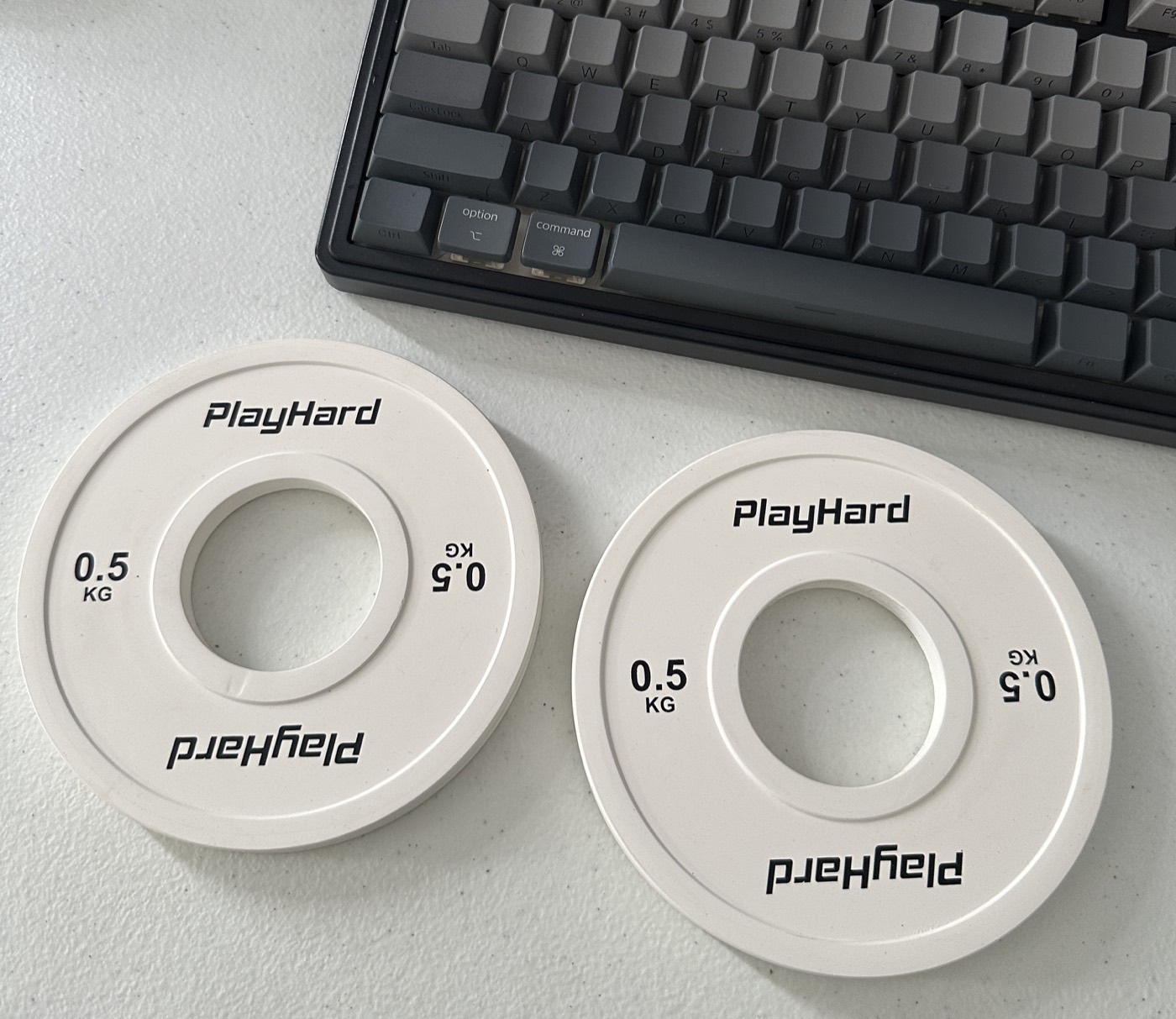 Two 0.5kg PlayHard weight plates sitting next to a mechanical keyboard